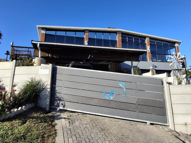 Front elevation of a multi-level house featuring a modern sliding driveway gate, paved driveway, and an elevated timber deck with extensive glass frontage.