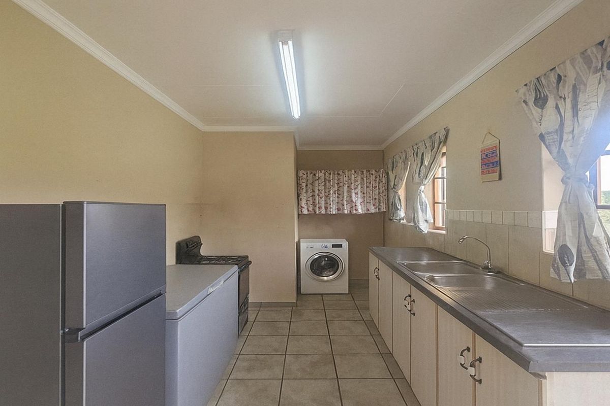 A functional kitchen featuring tiled flooring, built-in cabinetry, a double stainless steel sink, and space for laundry appliances.