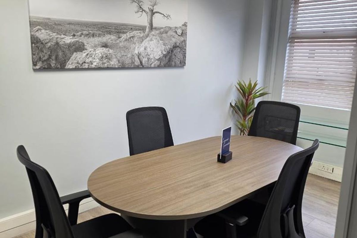 A professional office meeting room featuring laminate flooring, recessed lighting, and venetian blinds, providing a clean and functional workspace environment.