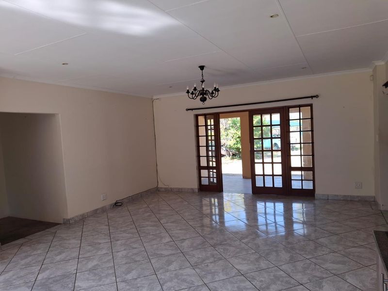 Spacious, empty living area featuring neutral walls, tiled flooring, and classic french doors leading to an outdoor space.