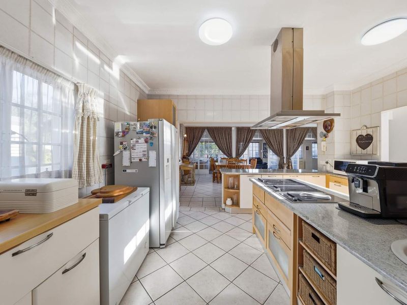 Spacious kitchen featuring a central island with built-in cooktop, extractor fan, ample cabinetry, and tiled finishes, flowing into an adjacent dining area.
