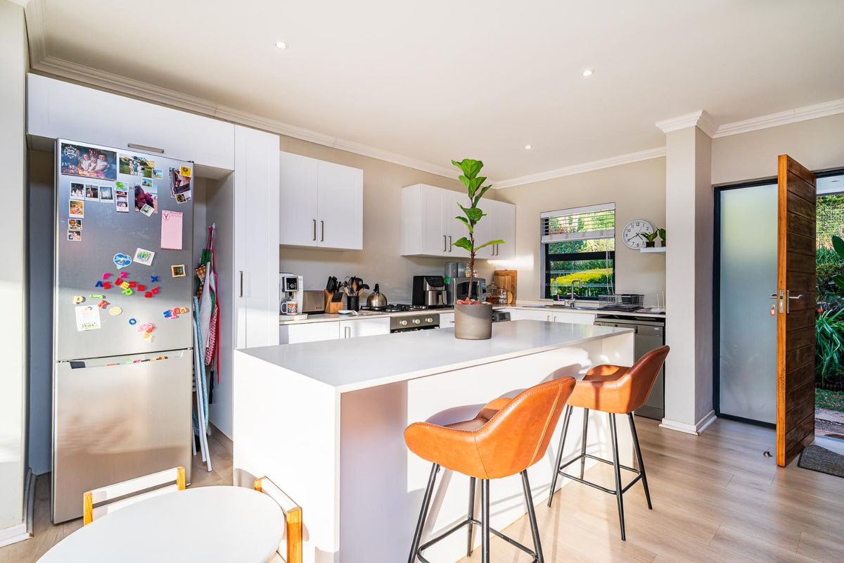 Modern kitchen featuring a central island with quartz countertops, white cabinetry, and integrated appliances, opening directly to an outdoor area.