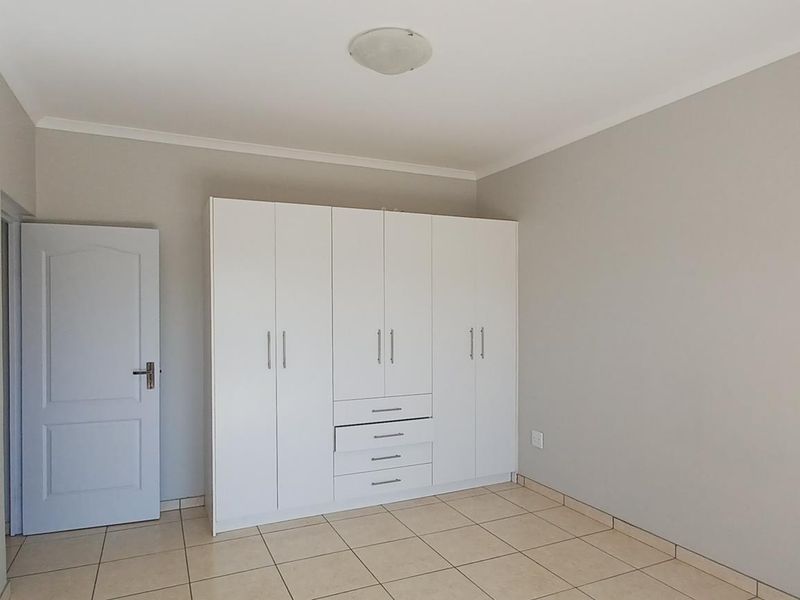 A clean, empty bedroom featuring neutral walls, tiled flooring, and a large white built-in wardrobe with integrated drawers.