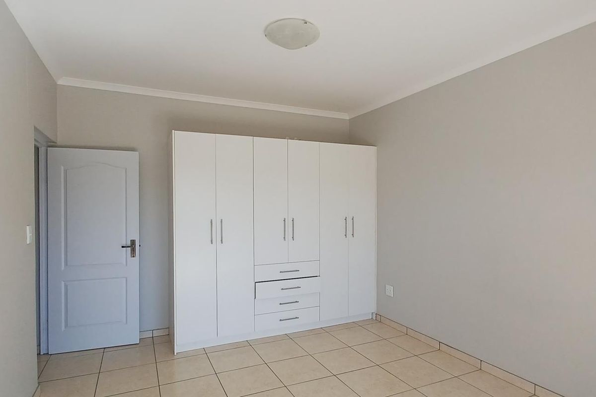 A clean, empty bedroom featuring neutral walls, tiled flooring, and a large white built-in wardrobe with integrated drawers.