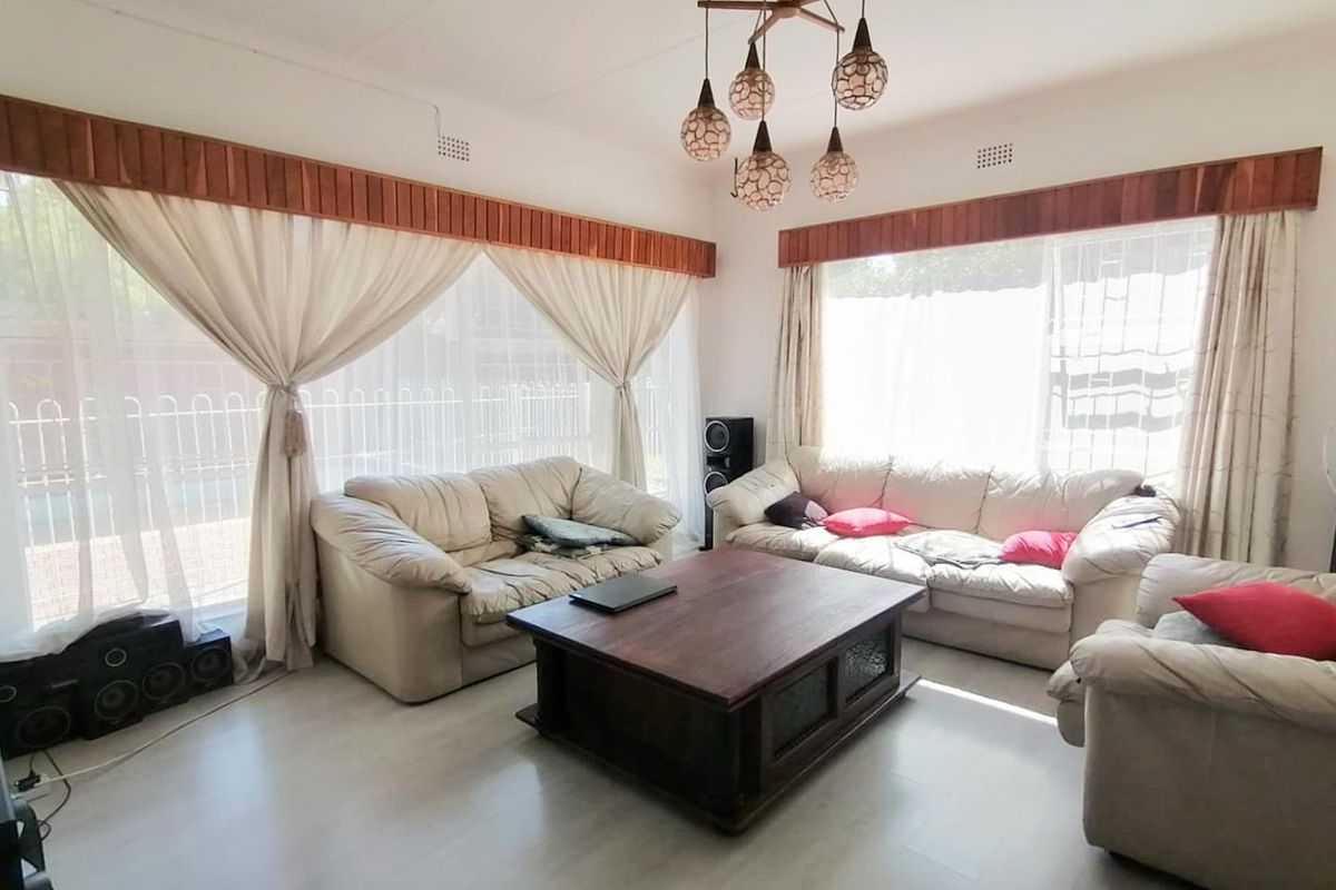 A bright living room featuring tiled flooring, large windows with wooden pelmets, and a decorative multi-pendant light fixture.
