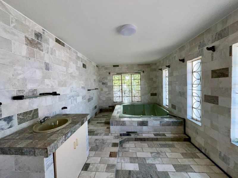 Spacious bathroom featuring stone wall and floor tiles, a built-in bathtub, and a vanity cabinet with an integrated sink.