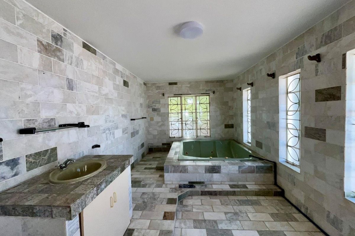 Spacious bathroom featuring stone wall and floor tiles, a built-in bathtub, and a vanity cabinet with an integrated sink.