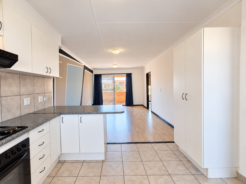 Open-plan kitchen and living area featuring white cabinetry, built-in oven, tiled and laminate flooring, and access to a balcony through a sliding door.