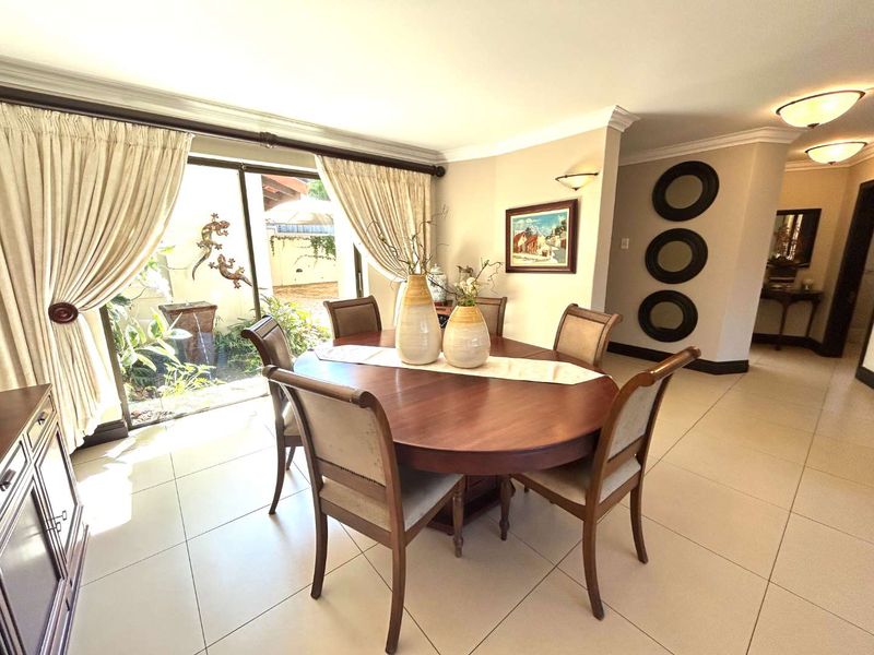 A bright dining room featuring large format floor tiles, crown molding, and a sliding glass door providing direct access to an outdoor patio area.