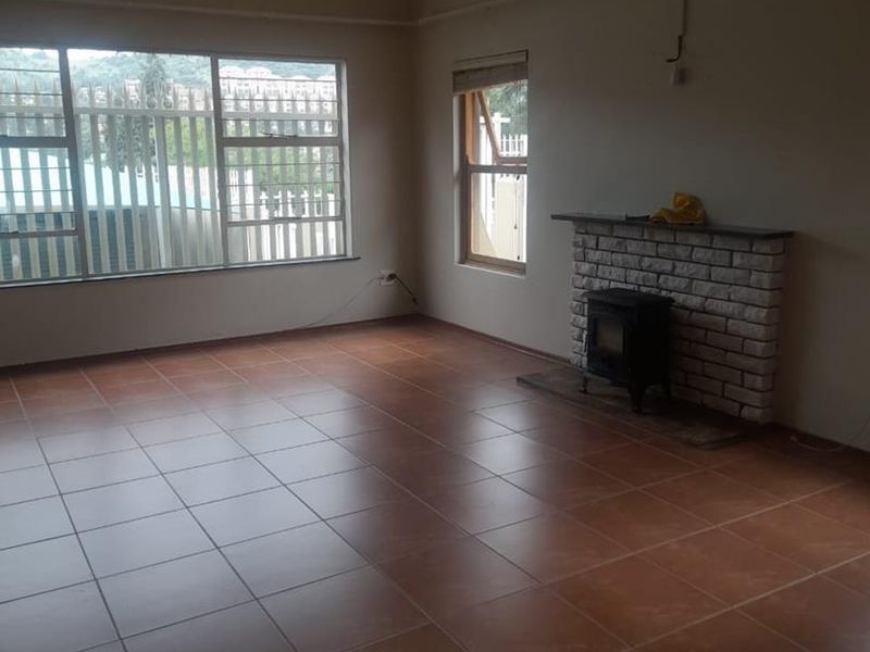 Spacious living room featuring tiled flooring, a brick fireplace with a wood-burning stove, and large windows with security bars.