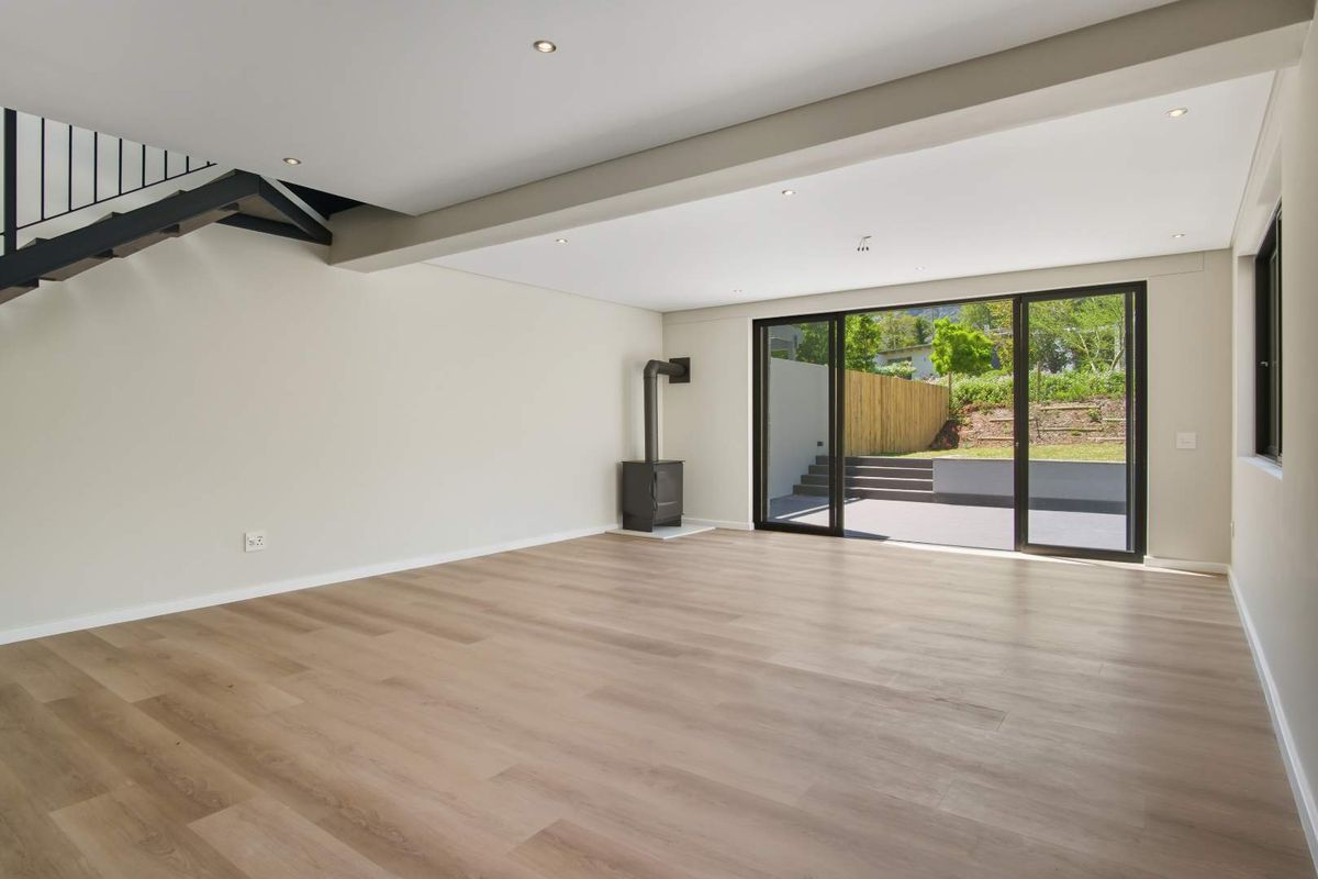 Spacious, modern living area featuring light wood-look flooring, a built-in wood-burning stove, and large sliding doors opening to a private rear patio.