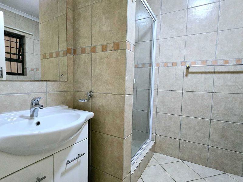 A functional bathroom featuring a vanity cabinet with a basin, a glass shower enclosure, and neutral wall and floor tiling.