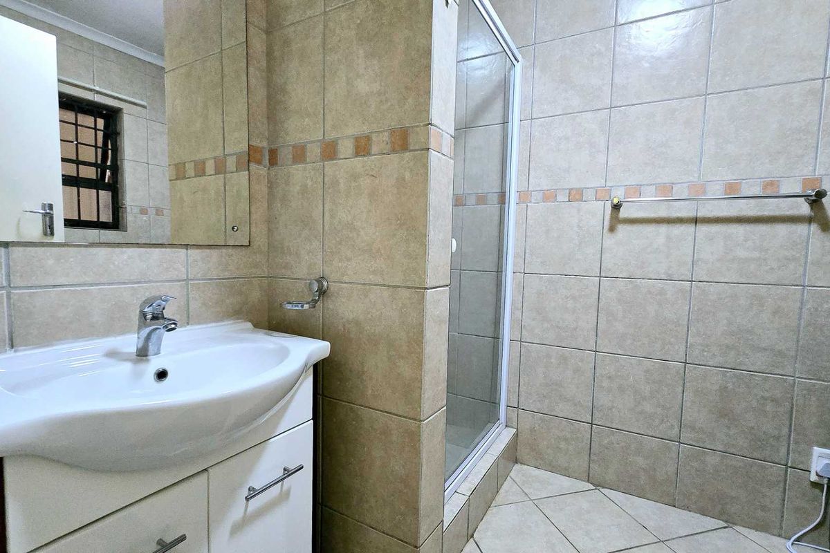 A functional bathroom featuring a vanity cabinet with a basin, a glass shower enclosure, and neutral wall and floor tiling.