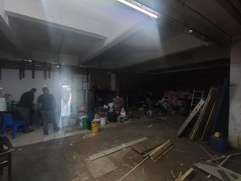 An industrial utility or storage space featuring exposed concrete ceilings, fluorescent lighting, and tiled flooring, currently used for general storage.