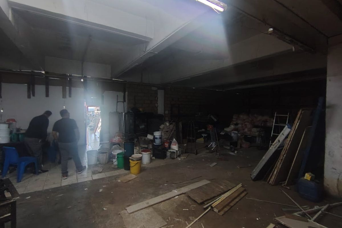 An industrial utility or storage space featuring exposed concrete ceilings, fluorescent lighting, and tiled flooring, currently used for general storage.