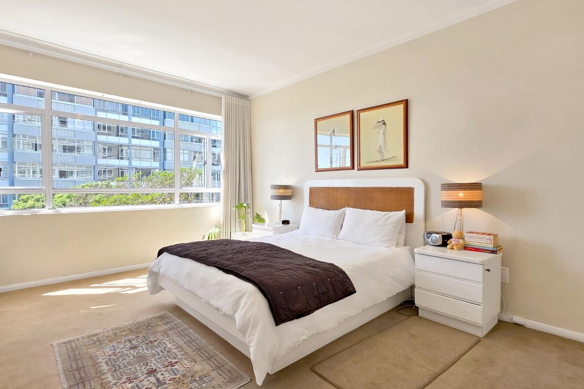A bright and spacious bedroom featuring large windows that provide ample natural light and a view of the surrounding apartment complex.