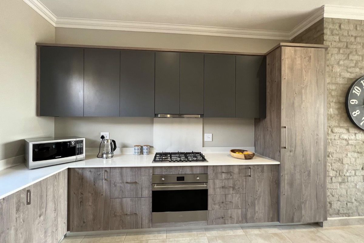 Modern kitchen featuring dark grey upper cabinetry, wood-grain lower cabinets, stone countertops, built-in oven, gas hob, and an extractor fan.