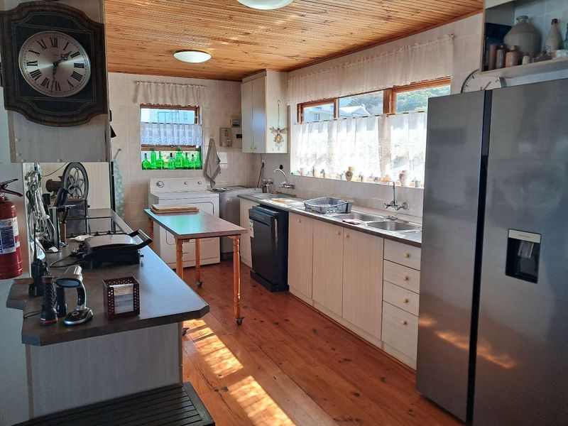 A functional kitchen featuring timber ceilings and flooring, ample cabinetry, laminate countertops, and a double stainless steel sink with natural light.