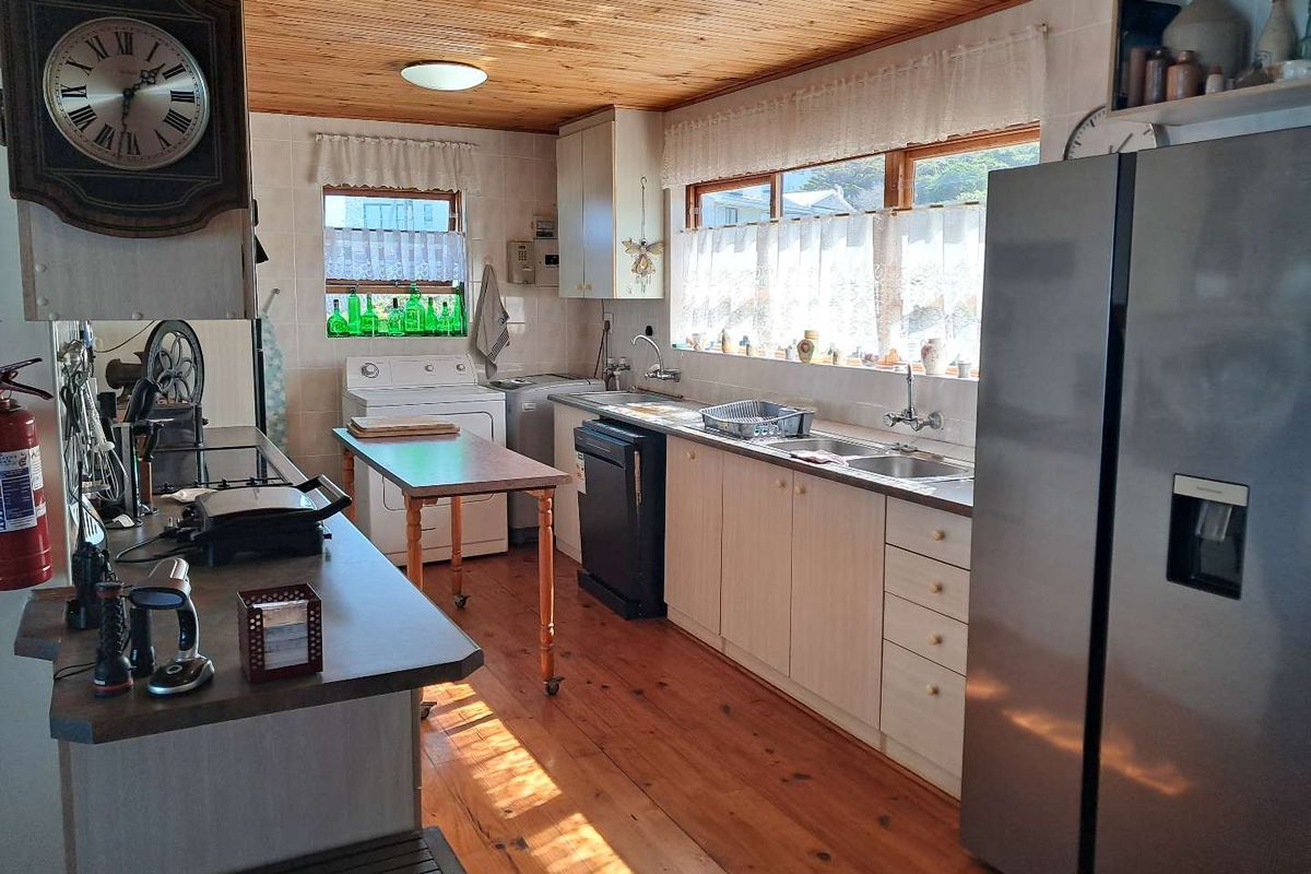 A functional kitchen featuring timber ceilings and flooring, ample cabinetry, laminate countertops, and a double stainless steel sink with natural light.