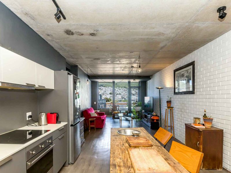 Modern open-plan apartment featuring an industrial-style exposed concrete ceiling, sleek kitchen cabinetry, and a bright living area leading to a balcony with city views.