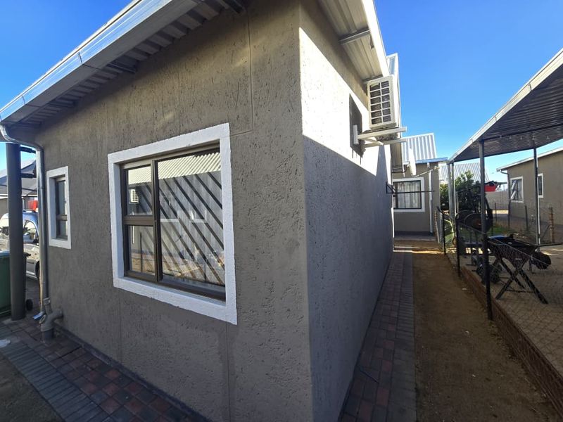 Side view of the apartment exterior featuring textured plaster walls, aluminium window frames with security bars, and a paved walkway.