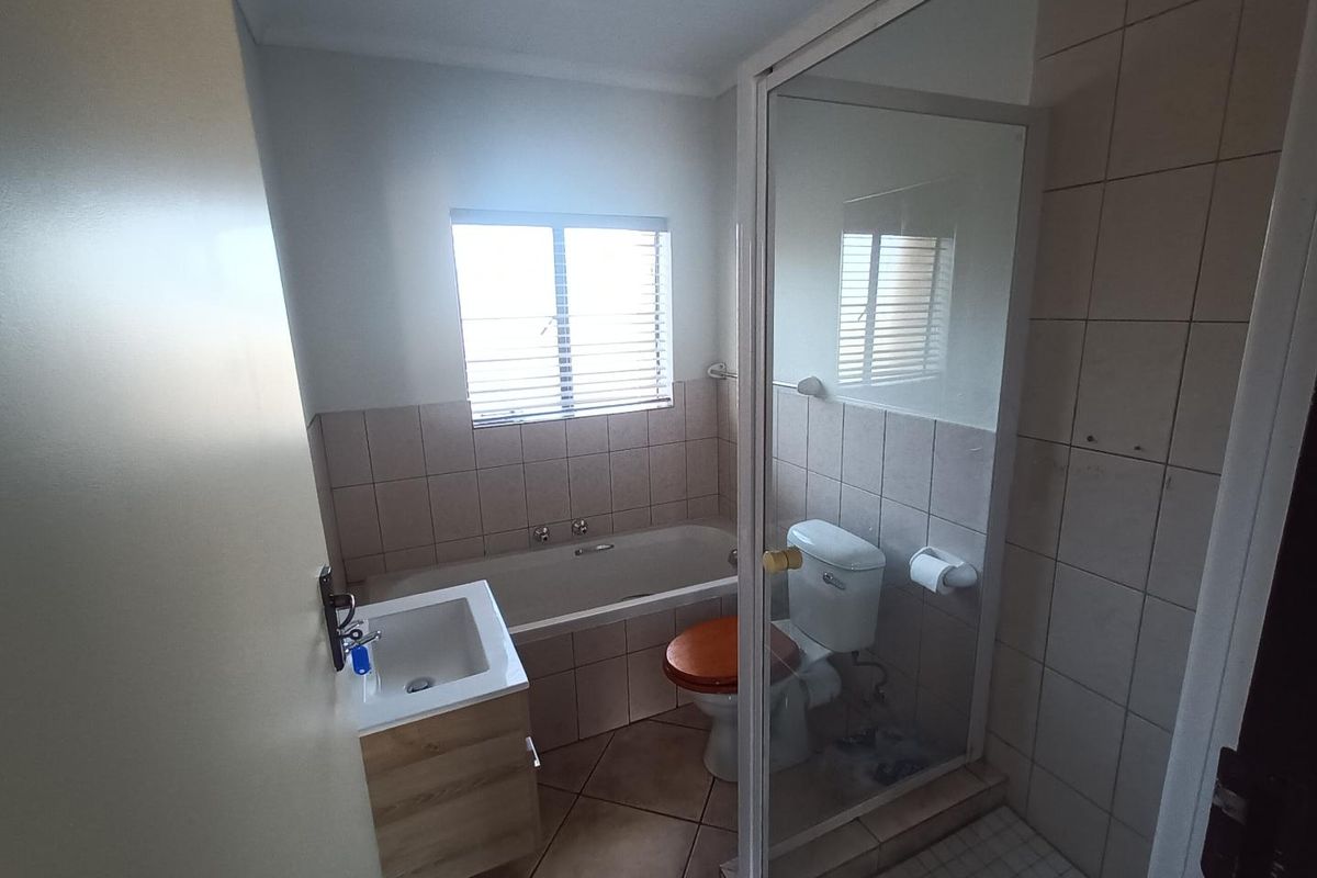 A functional bathroom featuring a built-in bathtub, a separate glass-enclosed shower, a vanity basin, and a toilet with tiled flooring and wall accents.