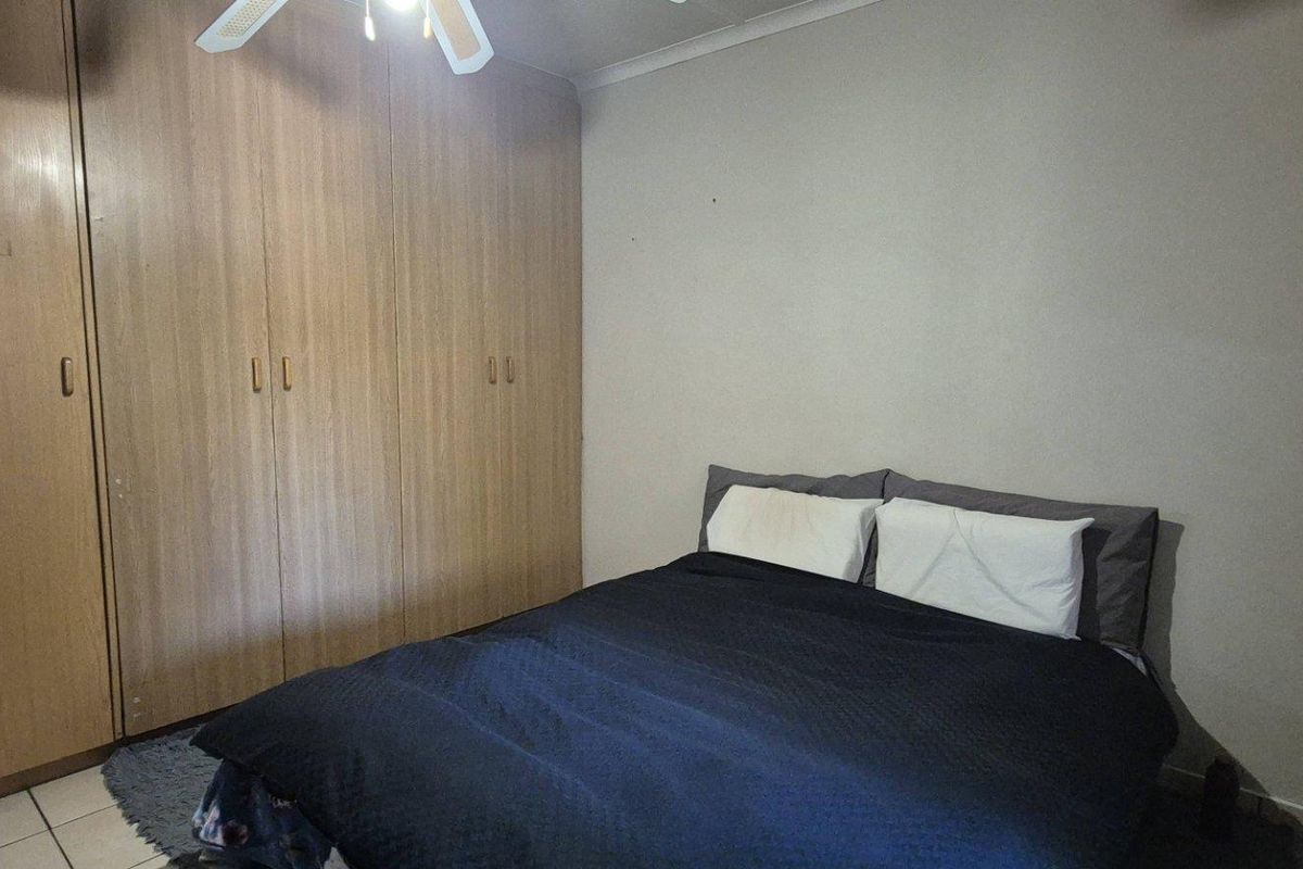 A bedroom featuring built-in wooden cupboards and a ceiling fan, providing functional storage and overhead lighting.