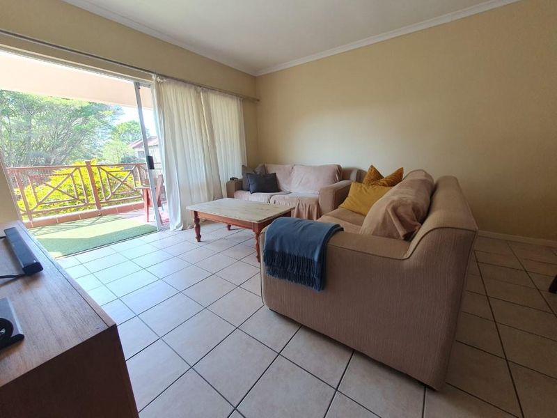 A bright living room featuring neutral tiled flooring and a large sliding glass door providing direct access to an outdoor balcony area.