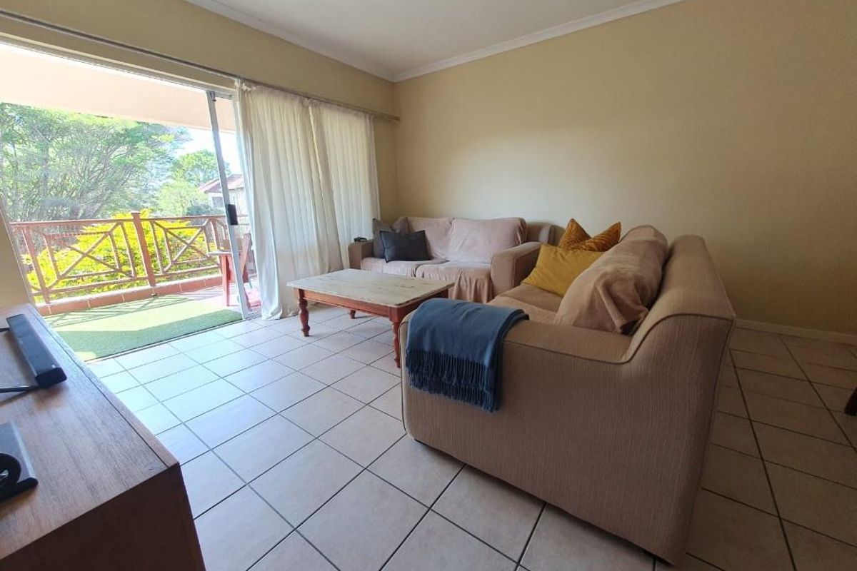 A bright living room featuring neutral tiled flooring and a large sliding glass door providing direct access to an outdoor balcony area.