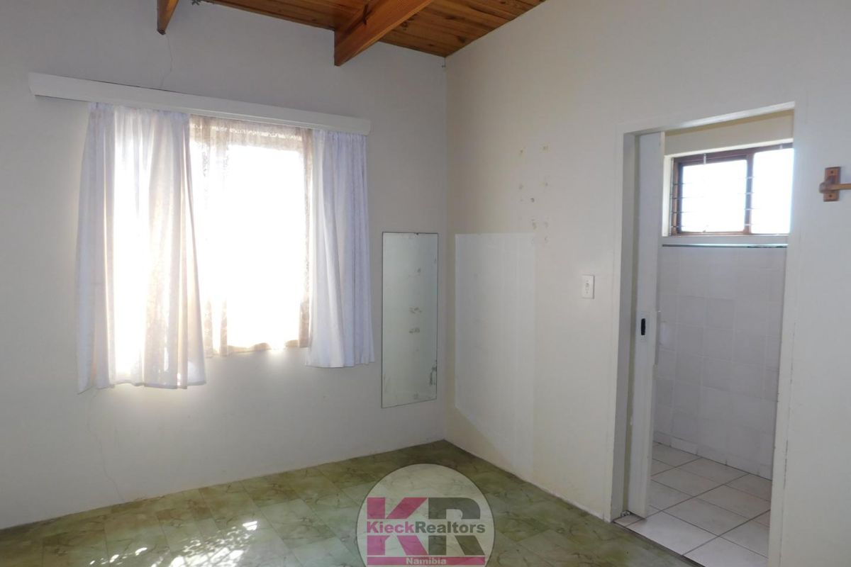 A bedroom featuring exposed timber ceiling beams, vinyl flooring, and an adjoining tiled bathroom area.
