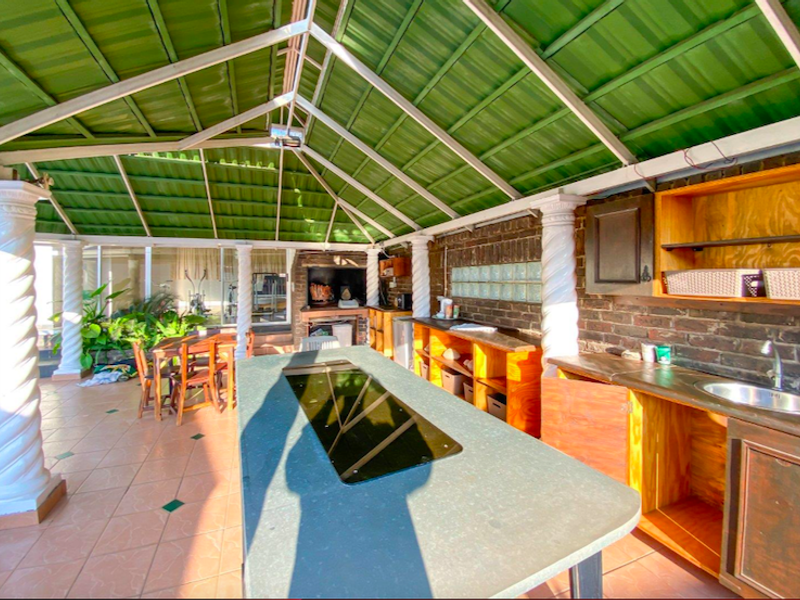 Covered outdoor patio featuring a built-in braai, kitchen prep area with sink, tiled flooring, and decorative columns, ideal for outdoor entertaining.