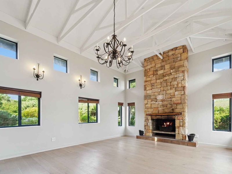 Spacious living room featuring a striking stone fireplace, vaulted ceilings with exposed rafters, timber flooring, and abundant natural light from multiple windows.