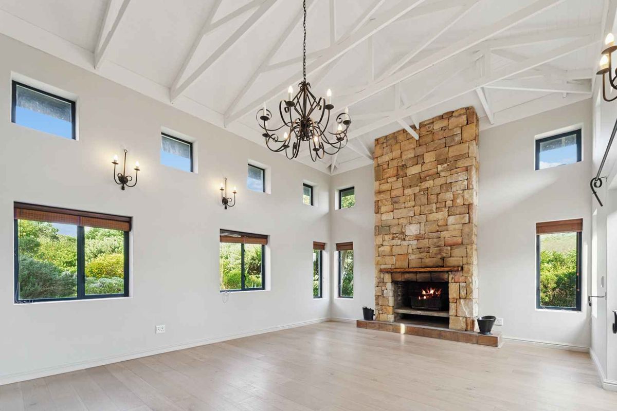 Spacious living room featuring a striking stone fireplace, vaulted ceilings with exposed rafters, timber flooring, and abundant natural light from multiple windows.