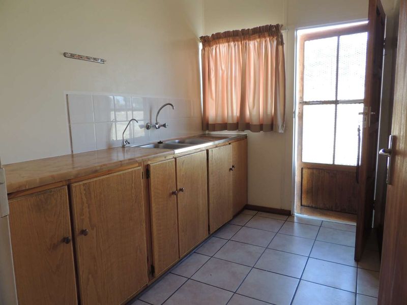 A functional scullery or utility area featuring wooden cabinetry, a double sink, tiled splashback, and direct access to the exterior.