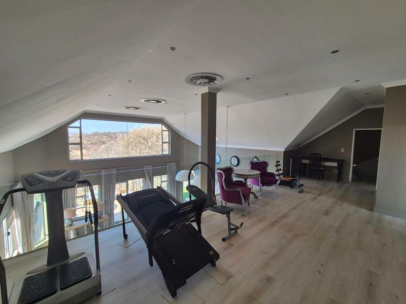 Spacious loft-style gym area featuring light wood-look laminate flooring, recessed lighting, and a large window offering scenic views.