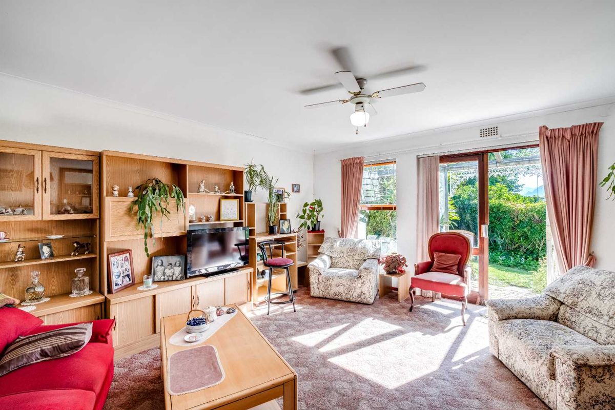 A spacious living room featuring a built-in wooden wall unit, ceiling fan, and sliding glass doors providing direct access to the rear garden.