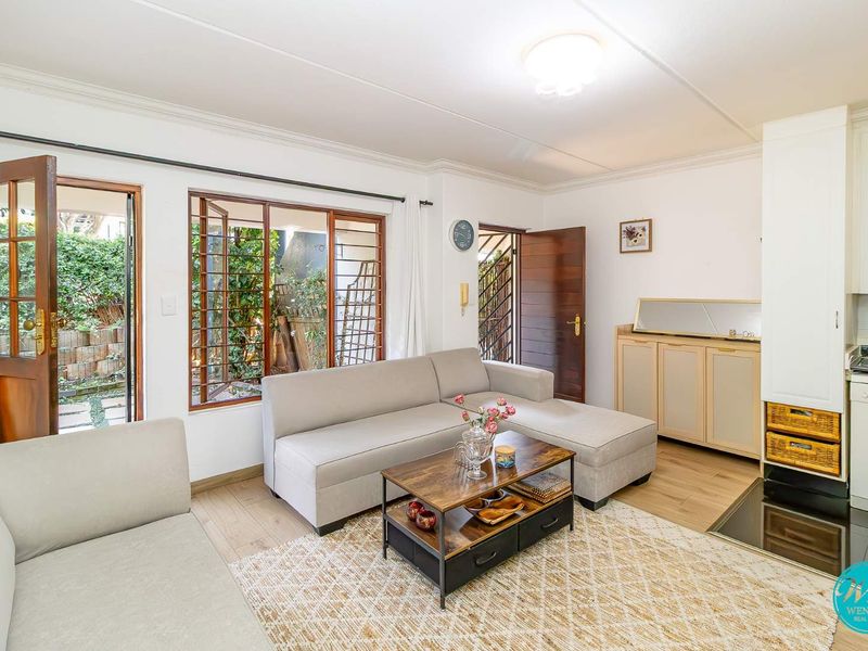 A bright living room featuring laminate flooring, timber-framed windows, and direct access to an outdoor area, creating a comfortable and functional living space.