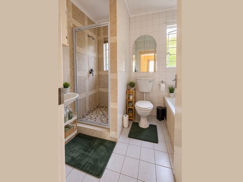 A functional bathroom featuring a separate shower enclosure, built-in bathtub, wall-mounted basin, and toilet with neutral tiled finishes throughout.
