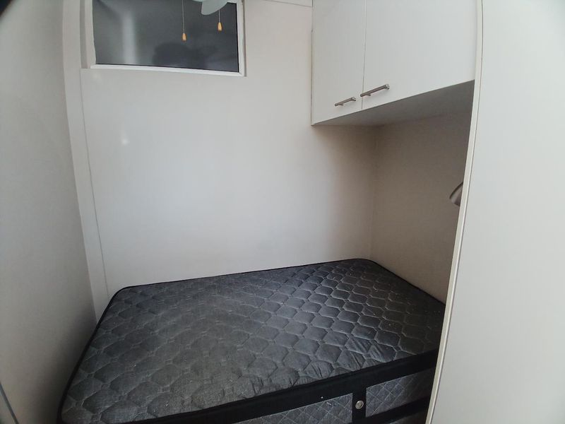 A compact bedroom featuring built-in overhead cabinetry and a high-level window for natural light.
