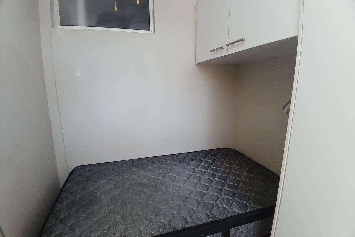 A compact bedroom featuring built-in overhead cabinetry and a high-level window for natural light.