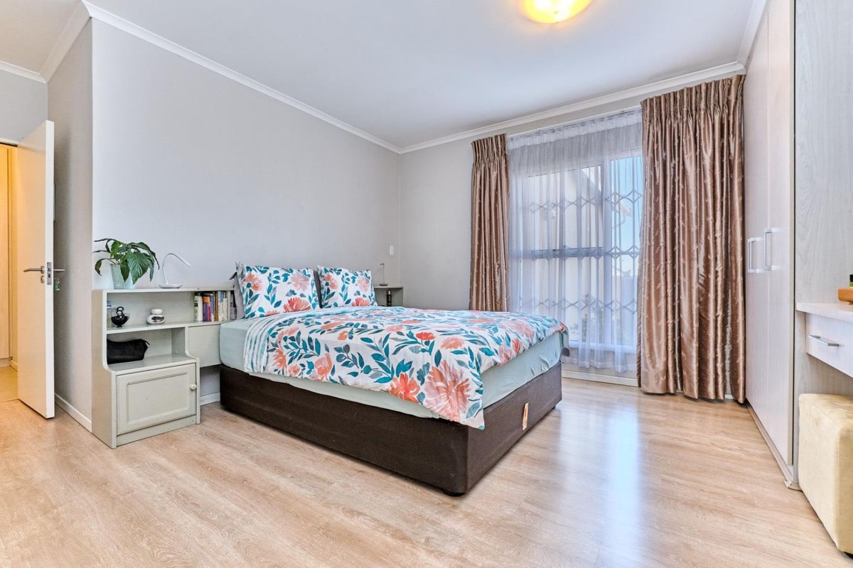 A well-maintained bedroom featuring light laminate flooring, a built-in wardrobe, and a window fitted with a security gate.