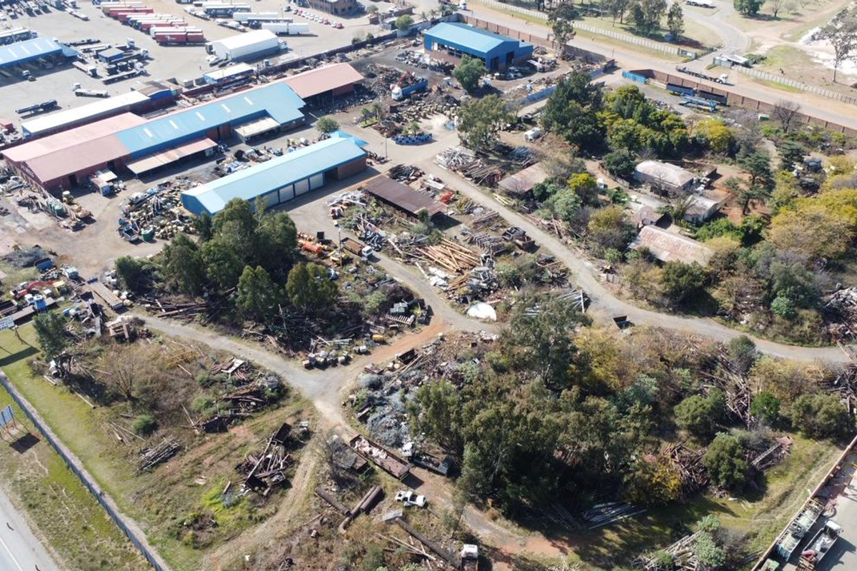 Aerial view of an industrial property featuring multiple warehouse structures, extensive open storage yard space, and perimeter fencing.