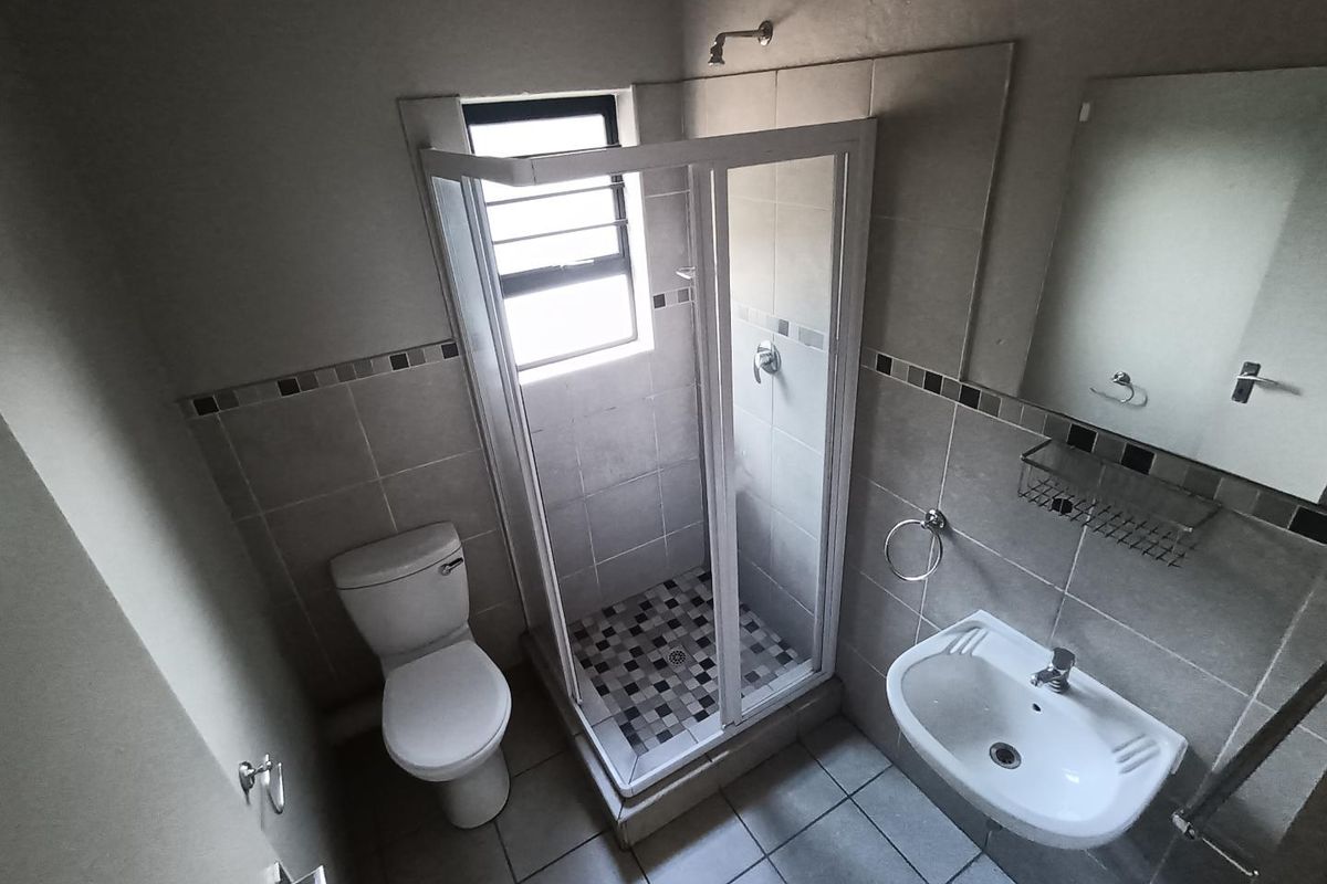 A functional bathroom featuring a shower enclosure, pedestal basin, and toilet with neutral wall and floor tiling.