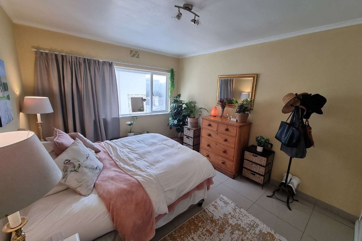 A cozy bedroom featuring tiled flooring, a ceiling-mounted spotlight fixture, and a large window allowing natural light into the space.