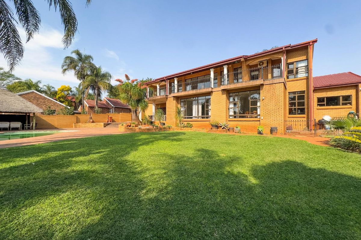 Spacious rear exterior view of a double-story brick house featuring a large manicured lawn, swimming pool, and an upper-level balcony.