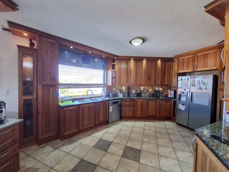 A spacious kitchen featuring extensive wooden cabinetry, granite countertops, tiled flooring, and integrated appliances, offering a functional and traditional layout.