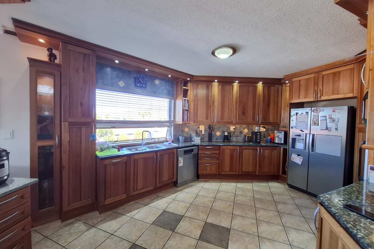 A spacious kitchen featuring extensive wooden cabinetry, granite countertops, tiled flooring, and integrated appliances, offering a functional and traditional layout.