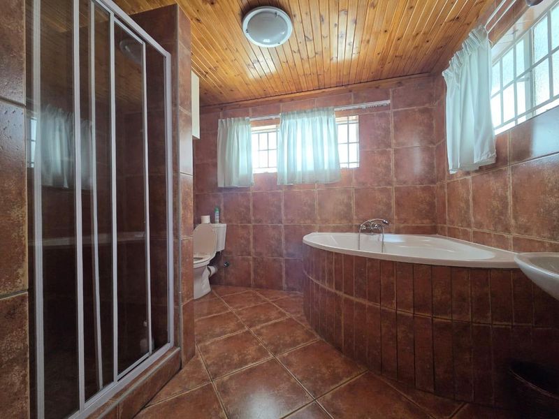 A bathroom featuring a corner bathtub, separate shower enclosure, toilet, and washbasin, finished with brown wall and floor tiles and a timber ceiling.