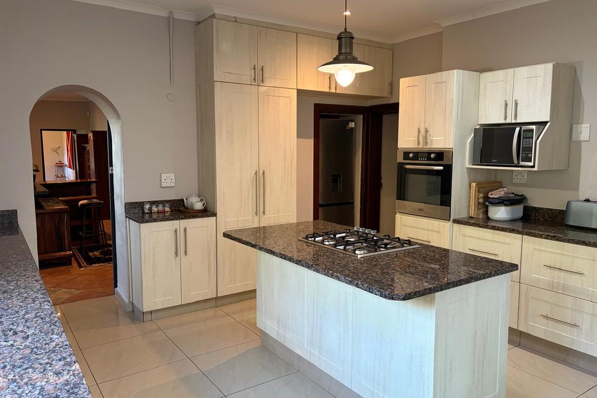 Modern kitchen featuring light wood cabinetry, granite countertops, a central island with a built-in gas hob, and integrated oven and microwave.