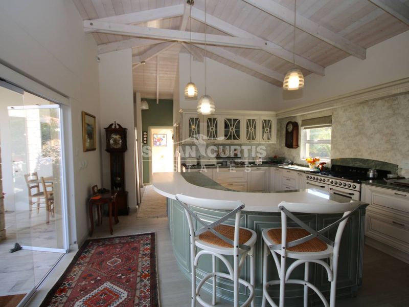 Spacious kitchen featuring a vaulted timber ceiling, curved breakfast bar, and integrated gas range, with direct access to the outdoor patio area.